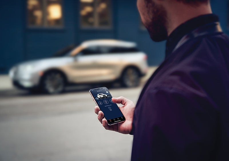 A person is shown interacting with a smartphone to connect to a Lincoln vehicle across the street. | J.C. Lewis Lincoln in Savannah GA