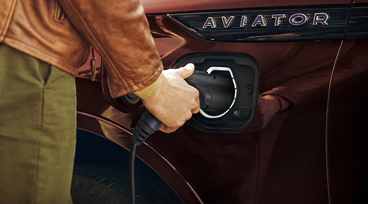 A hand is shown plugging a charger into the charging port of a 2023 Lincoln Aviator® Plug-in Hybrid model. | J.C. Lewis Lincoln in Savannah GA