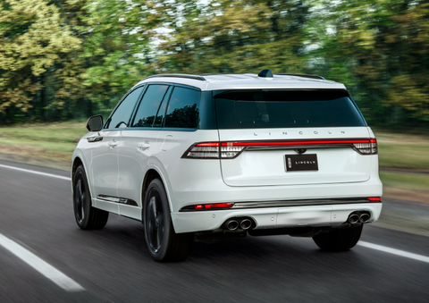 A white 2025 Lincoln Aviator® SUV is being driven away down a road lined with colorful trees. | J.C. Lewis Lincoln in Savannah GA