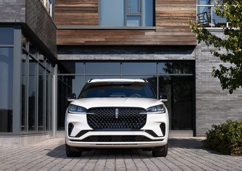 A white 2025 Lincoln Aviator® SUV is shown parked outside a modern building with gray brick and wood accents. | J.C. Lewis Lincoln in Savannah GA
