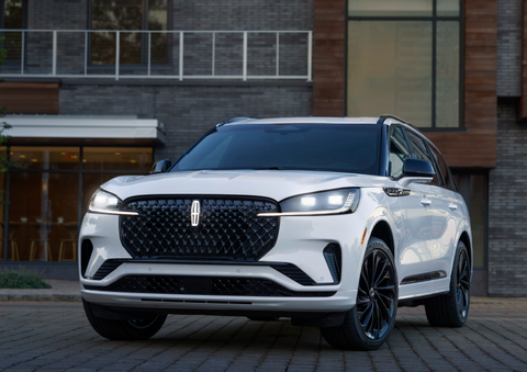 A white 2025 Lincoln Aviator® SUV is shown parked outside a modern building with gray brick and wood accents. | J.C. Lewis Lincoln in Savannah GA