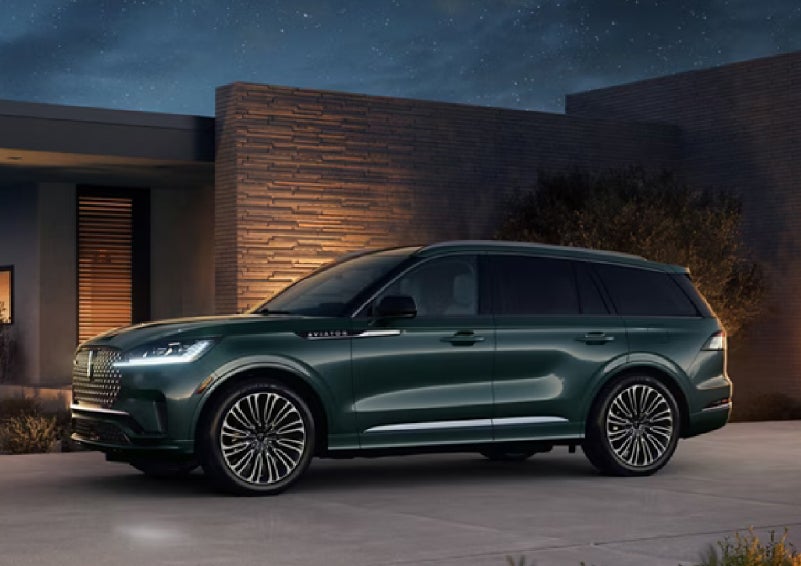 A green 2027 Lincoln Aviator® SUV is parked outside a contemporary home. | J.C. Lewis Lincoln in Savannah GA