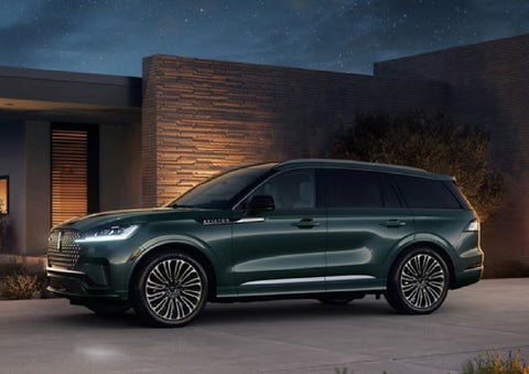A green 2027 Lincoln Aviator® SUV is parked outside a contemporary home. | J.C. Lewis Lincoln in Savannah GA